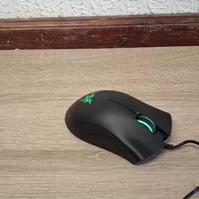 Rato de gaming preto com luzes verdes sobre superfície de madeira clara