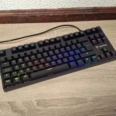 Teclado mecânico preto com iluminação RGB sobre mesa de madeira clara
