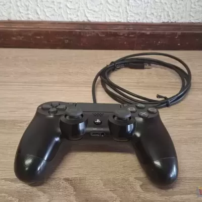 Comando de videojogo preto com cabo sobre mesa de madeira clara