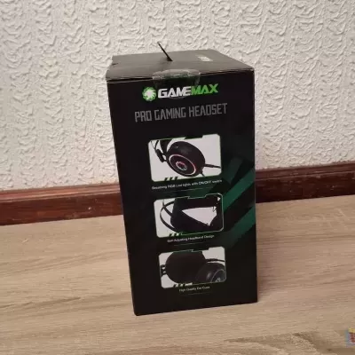 Caixa de headset GAMEMAX preto com texto e imagens do produto junto a uma parede branca.