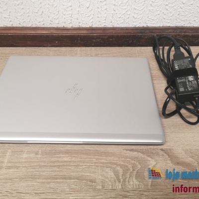 Portátil HP prateado fechado com carregador preto ao lado sobre madeira clara