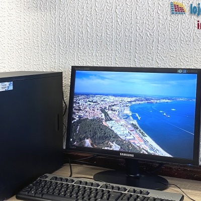 Computador desktop com torre Tsunami e monitor Samsung a mostrar imagem aérea de cidade e mar