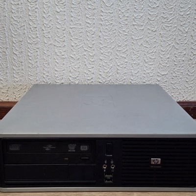 Computador de secretária preto e cinza da marca HP em chão de madeira junto a parede branca