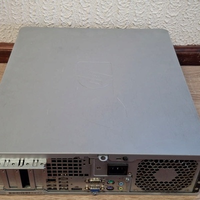 Computador de secretária cinza visto pela parte traseira num chão de madeira.