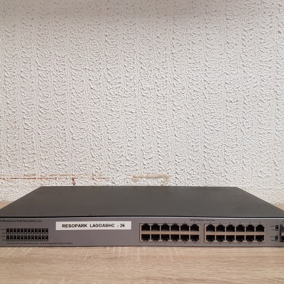 Switch de rede preto com 24 portas Ethernet e 4 portas SFP em superfície de madeira