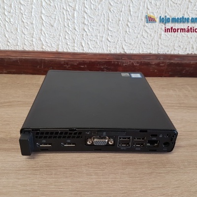 Computador compacto preto com portas traseiras visíveis sobre chão de madeira em parede branca texturada