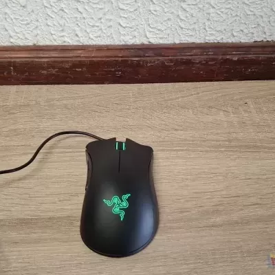 Rato gaming preto com símbolo iluminado em verde sobre chão de madeira