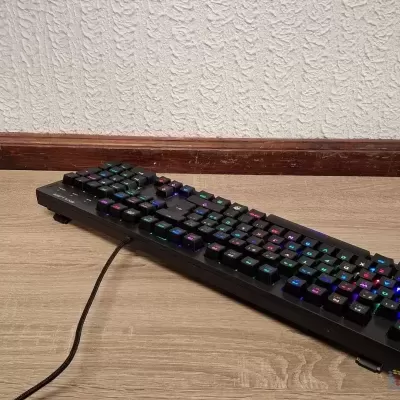 Teclado mecânico compacto preto com luzes RGB sobre piso de madeira