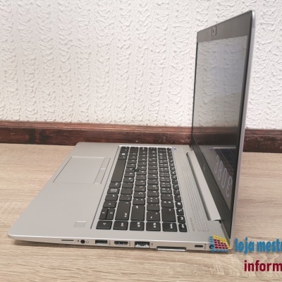 Portátil prateado com teclado preto e várias portas laterais numa superfície de madeira clara.