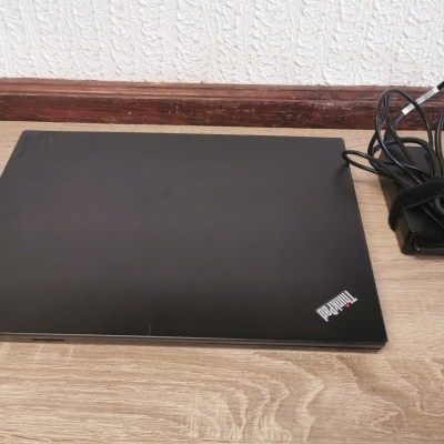 Portátil preto Lenovo ThinkPad fechado sobre mesa de madeira com carregador ao lado