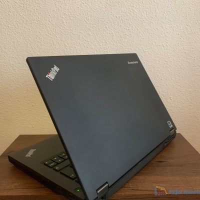 Computador portátil preto Lenovo ThinkPad parcialmente aberto sobre mesa de madeira clara