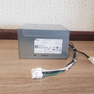 Fonte de alimentação Dell cinza com autocolante na superfície de madeira e parede branca ao fundo