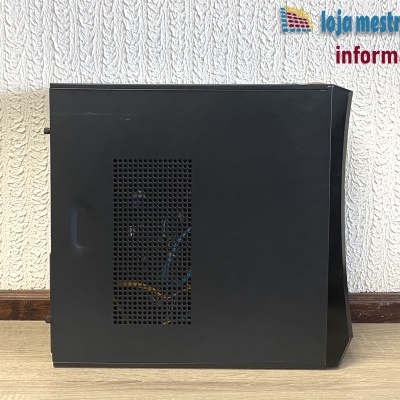 Computador preto com lateral perfurada, em chão de madeira e parede branca texturada de fundo