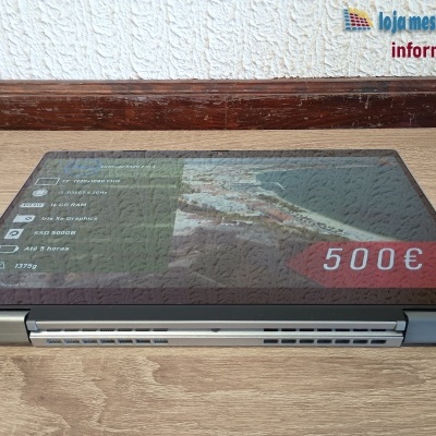 Computador portátil Dell Latitude 7330 2 em 1 prateado fechado sobre mesa de madeira com informações técnicas no ecrã.