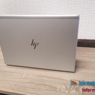 Portátil HP prateado fechado sobre mesa de madeira, parede branca ao fundo