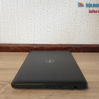 Computador portátil preto Dell fechado sobre mesa de madeira clara com fundo de parede branca texturada