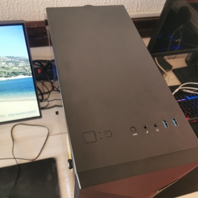 Torre de computador preta com portas e botões, perto de dois monitores numa secretária