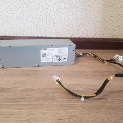 Fonte de alimentação Dell cinza com cabos pretos sobre chão de madeira