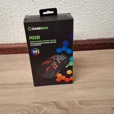 Caixa de rato gaming GameMax M68 em chão de madeira clara junto a parede branca.