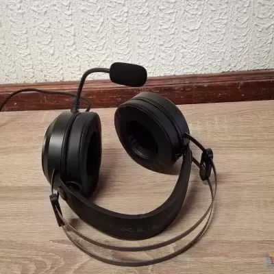 Auscultadores negros com microfone em fundo de chão de madeira clara e parede branca