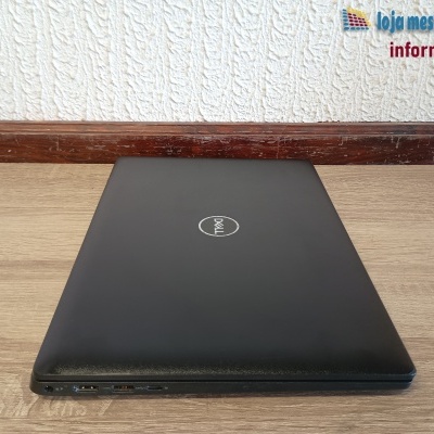 Computador portátil Dell preto fechado sobre mesa de madeira clara com parede branca texturizada ao fundo