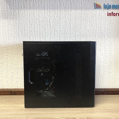 Computador desktop preto com ventoinhas visíveis lateralmente sobre chão de madeira