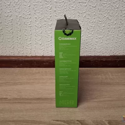 Caixa verde e preta da marca OMSENMAX numa sala com chão de madeira e parede branca