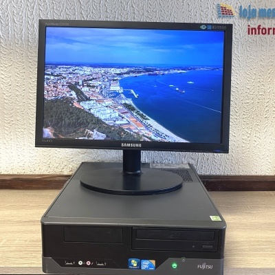 Computador de secretária preto com monitor Samsung a mostrar imagem aérea costeira.