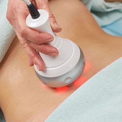 Dispositivo branco com luz vermelha em pele do abdômen com toalha verde clara