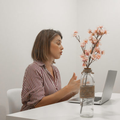 Vidro decorativo com flores artificiais rosa numa mesa branca junto a um portátil
