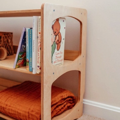 Estante de madeira clara com livros infantis e um cobertor laranja dobrado