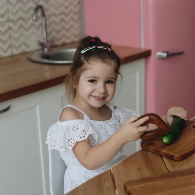 Criança na cozinha com pepino e frigorífico rosa