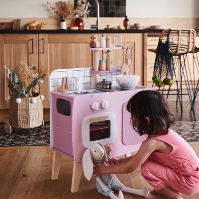 Cozinha de brincar rosa com forno e fogão e uma criança a brincar no chão
