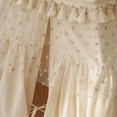 Detalhe de tecido transparente bege com bolinhas douradas e franjas decorativas.