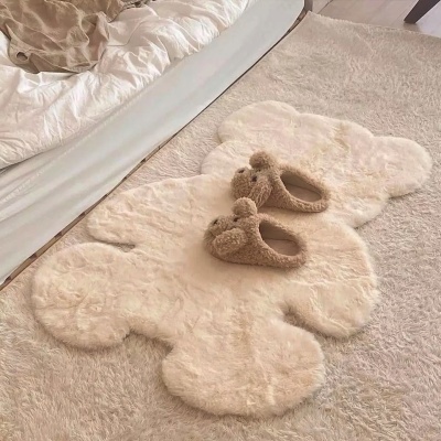 Tapete branco peludo em forma de nuvem com chinelos castanhos peludos em cima próximo a uma cama