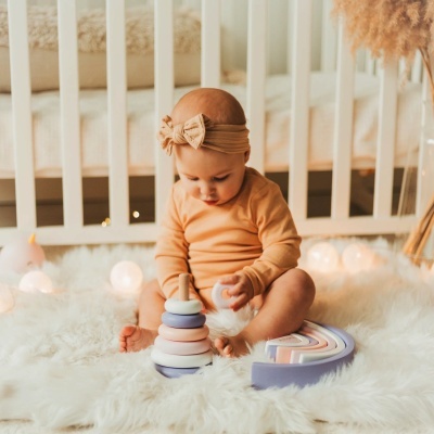 Bebé com roupa cor de pêssego a brincar com brinquedos de empilhar e arco-íris em tapete branco