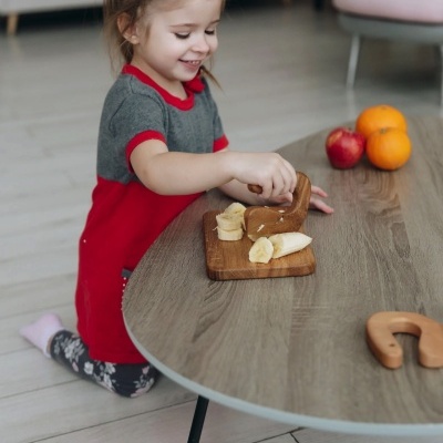 Menina pequena a comer frutas num tabuleiro de madeira sobre uma mesa cinzenta de madeira
