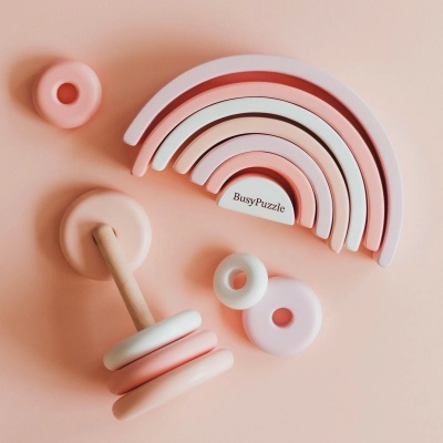 Conjunto de brinquedos de madeira e silicone coloridos em tons pastel, com arco-íris e anéis empilháveis sobre superfície cor de pêssego