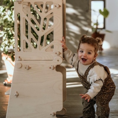 Móvel infantil em madeira clara com padrões vazados e criança pequena a brincar