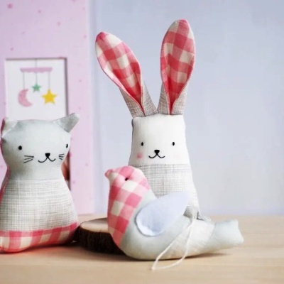 Três peluches de tecido com padrão xadrez cor-de-rosa e branco: gato, coelho e pássaro sobre mesa de madeira