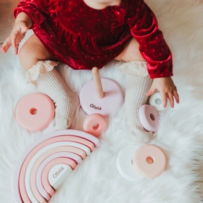 Bebé com vestido vermelho e meias bege brinca com brinquedos de madeira rosa e branco