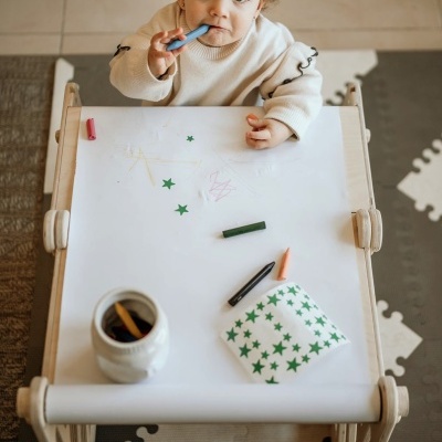 Mesa infantil com materiais de desenho e uma criança desenhando
