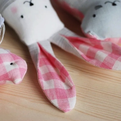 Três brinquedos de pano em forma de coelhos com orelhas em tecido xadrez e azul claro sobre madeira