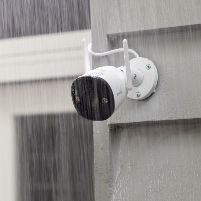 Câmara de vigilância branca e preta da marca imou montada numa parede cinza molhada pela chuva