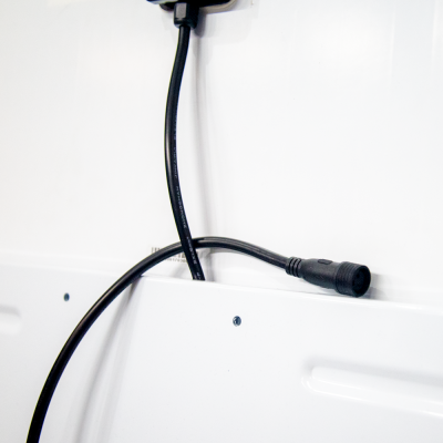 Cabo preto com conector circular sobre superfície branca com parafusos e etiqueta