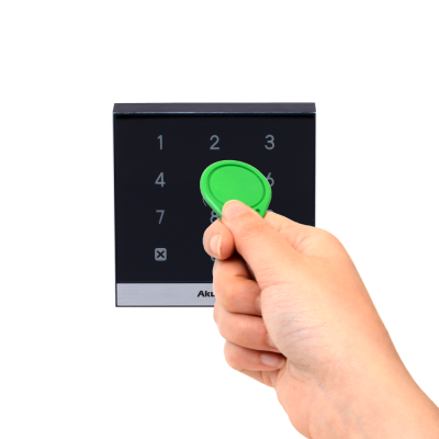 Mão segura dispositivo verde junto a painel numérico preto com números e botão X