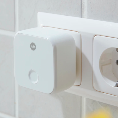 Dispositivo branco Yale ligado a tomada elétrica em azulejos cinza