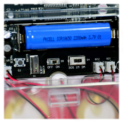Placa eletrónica com bateria azul e componentes, interruptores e fios vermelhos e pretos.