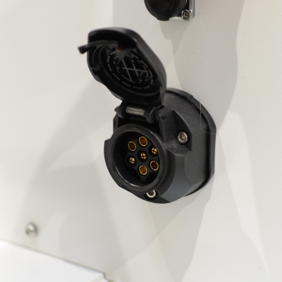 Tomada elétrica preta de 5 pinos com tampa aberta numa parede branca