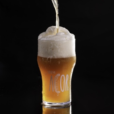 Copo de cerveja com espuma sendo servido de garrafa, com o texto 'AÇOR' no copo